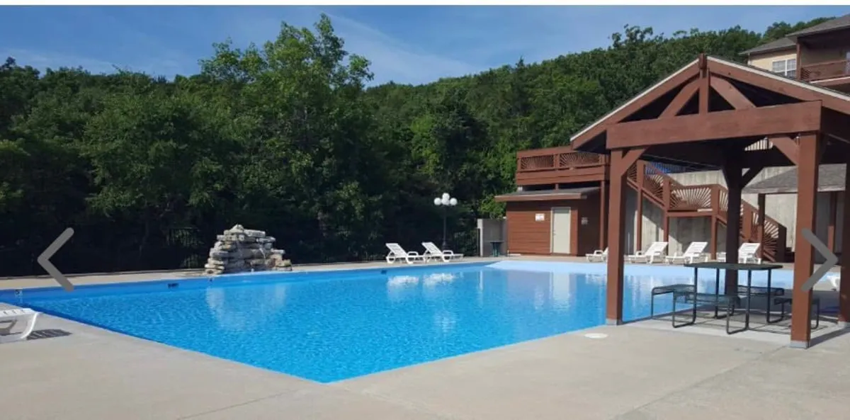 A refreshing outdoor pool scene with a swimming pool, wooden gazebo, lounge chairs, and a decorative rock fountain. The area invites both relaxation and social activities, representing resort-style amenities.