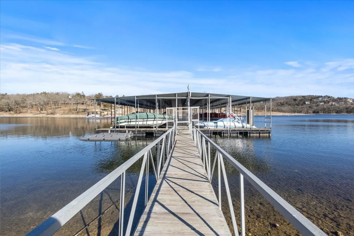 A serene exterior view of a dock extending into the clear water, with multiple boats moored along its sides and a vast sky overhead. The scene is tranquil, perfect for early morning fishing trips, and highlights direct lake access.