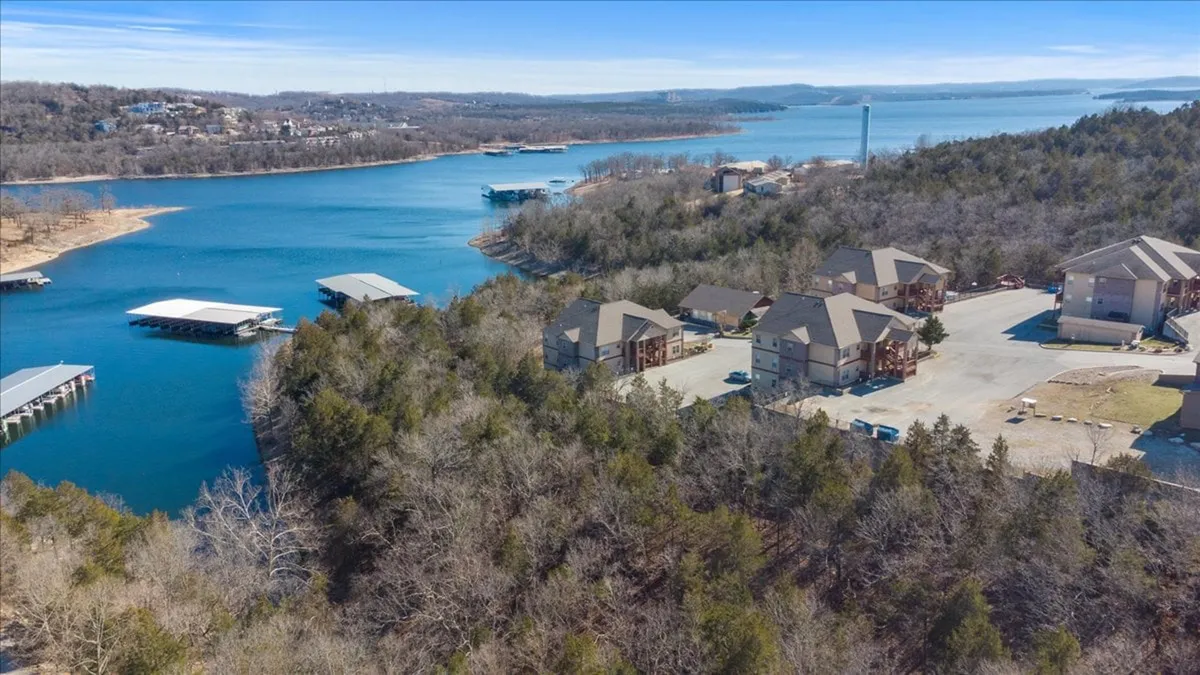 A tranquil lakeside scene featuring a shimmering lake, docks that stretch into the water, lush trees along the shoreline, and residential buildings set back from the water’s edge. The image shows ample space for boating, fishing, and swimming, with hints of people enjoying lakeside activities in a relaxed atmosphere.