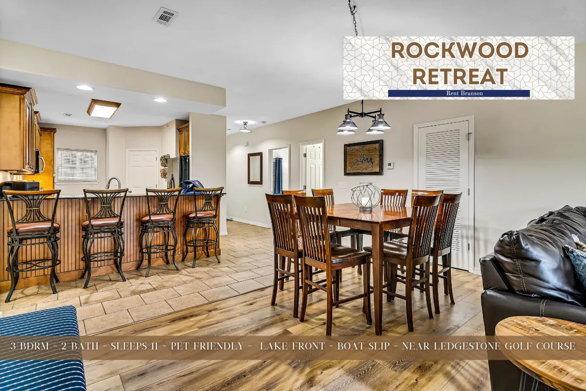 A welcoming view of the dining table, bar stools, and kitchen area set under warm lighting fixtures. The scene is arranged for family dinners, game nights, and shared meals, capturing the communal spirit with the kitchen integrated into the space.