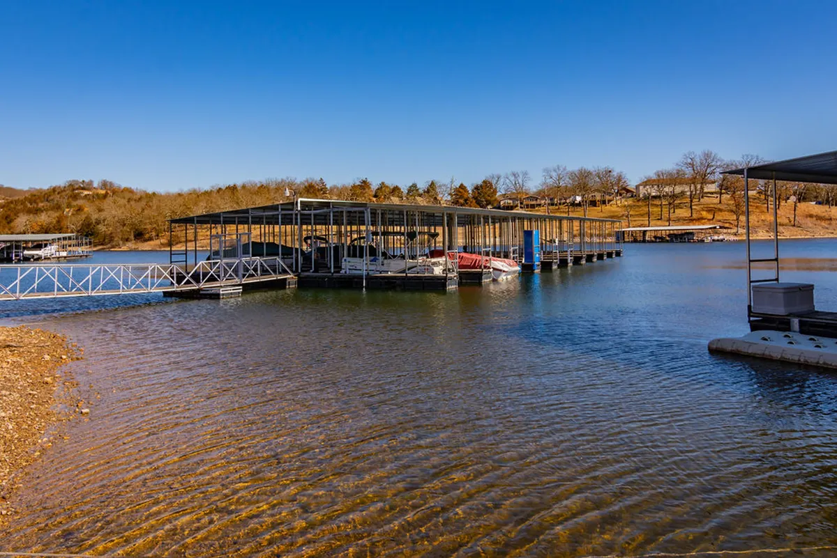 An inviting dock scene with the water’s surface glimmering in the sun, surrounded by trees and nature. The dock looks perfect for fishing, swimming, or simply enjoying the view, with a tranquil and welcoming mood.