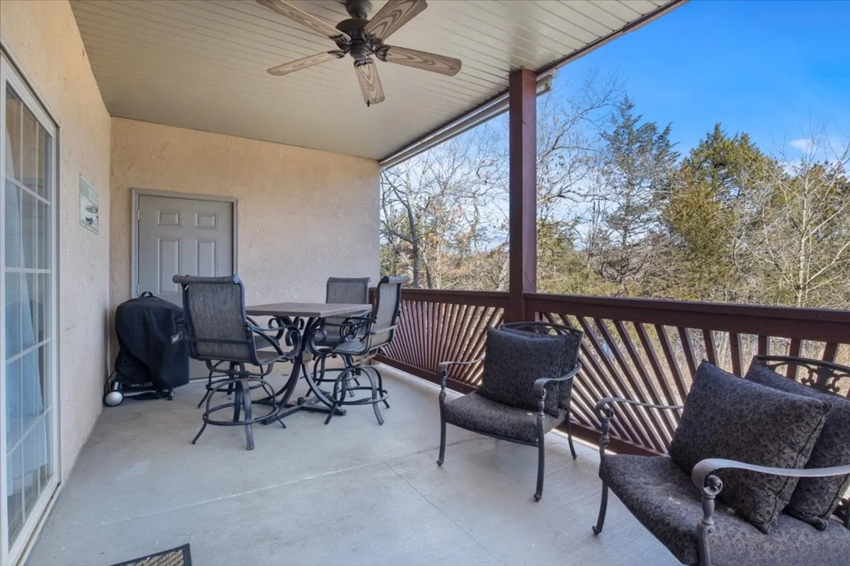 An inviting outdoor dining area with comfortable seating, a decorative railing, and a ceiling fan, overlooking natural surroundings. The space is set for group meals, relaxation, and socializing in the open air.