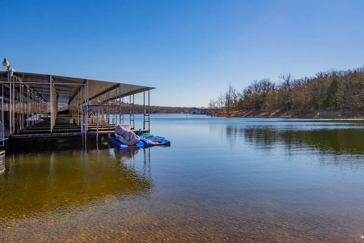 A peaceful lakeside setting with a boat dock stretching across the water, surrounded by mature trees. The tranquil environment hints at easy access to outdoor adventures and serene relaxation by the lake.