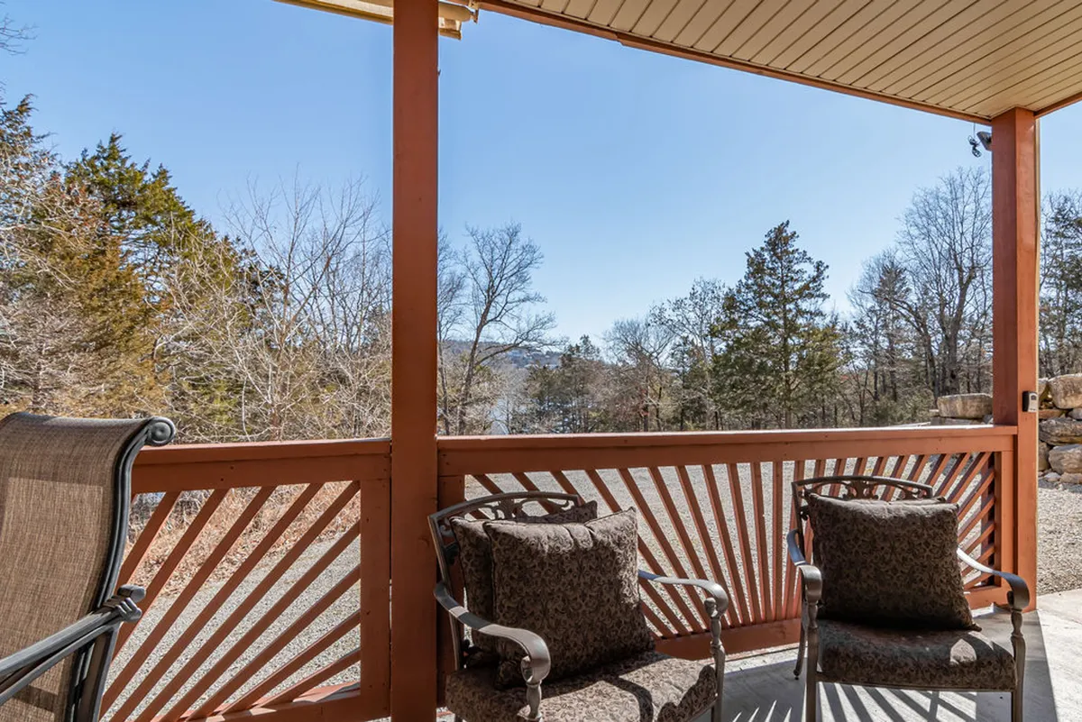 A serene lakeside deck featuring comfortable seating and a wooden railing with breathtaking views of Table Rock Lake just beyond. The setting is ideal for relaxing, reading, or enjoying the natural surroundings, with the sense of being steps from the water.