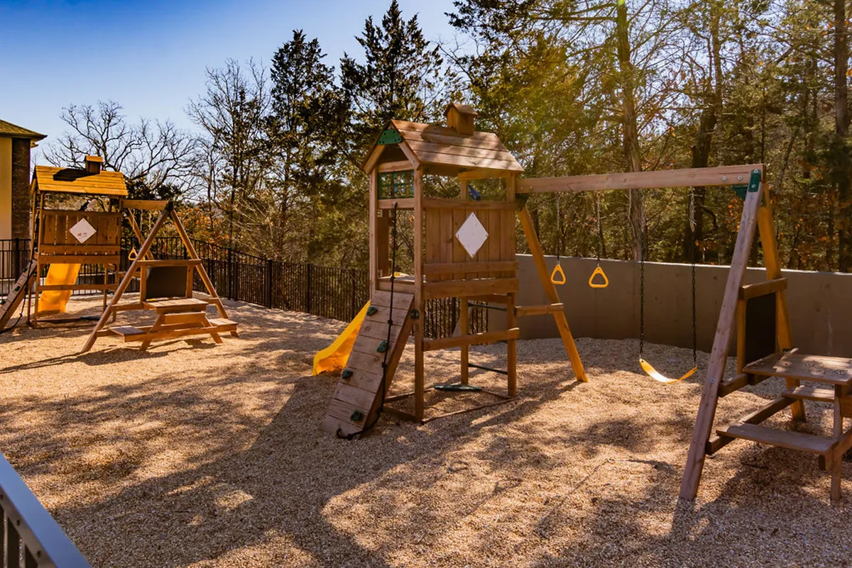 A cheerful playground with a swing set and play structure set in a sandy area, surrounded by open space for families and children to gather and play.